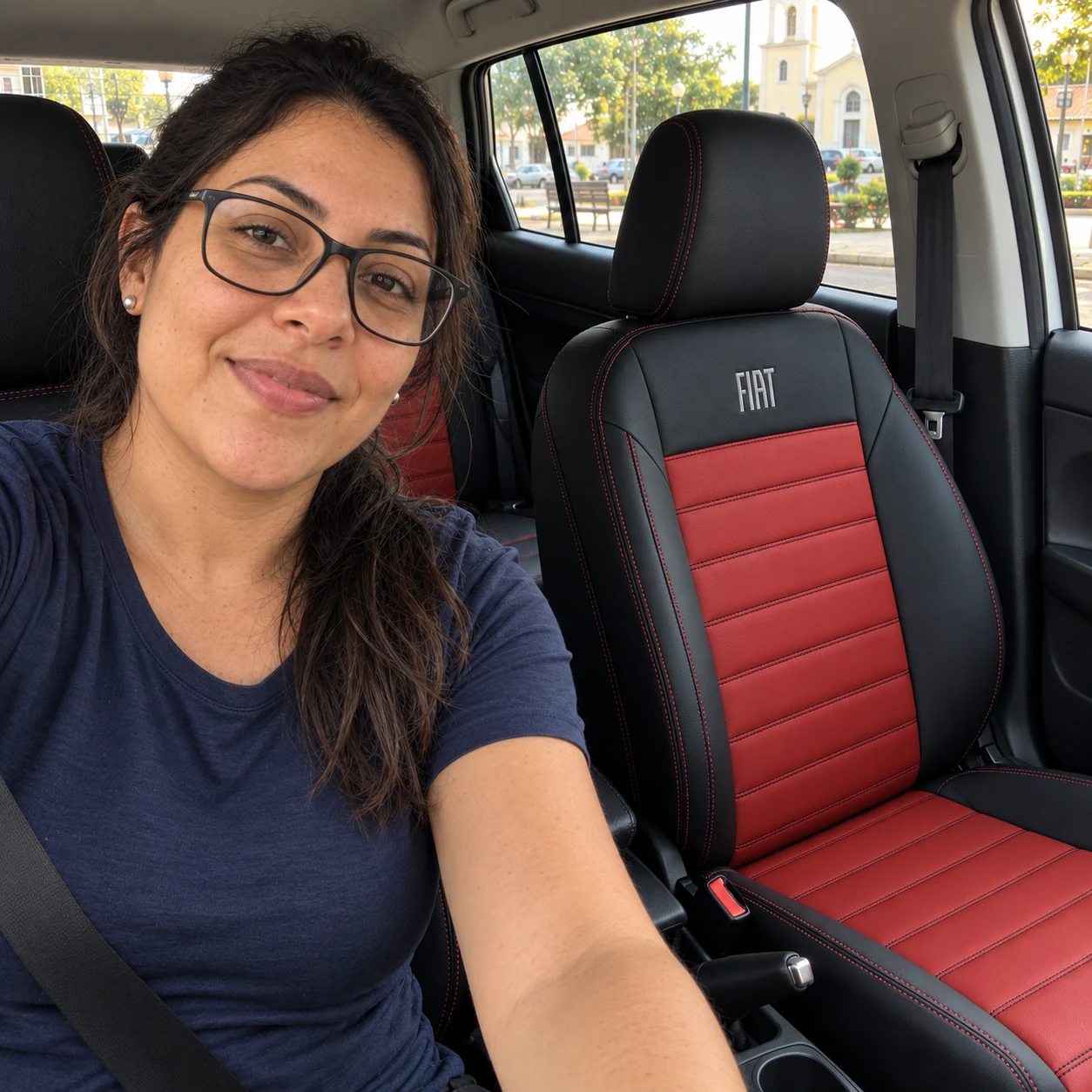 Juliana de óculos e camiseta azul no Fiat Cronos com bancos Clássico pretos com centro vermelho e logo Fiat bordada